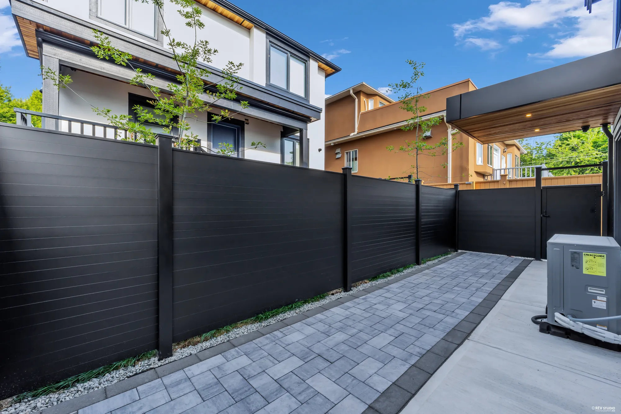 The paved patio alongside the house with the heat pump at the end